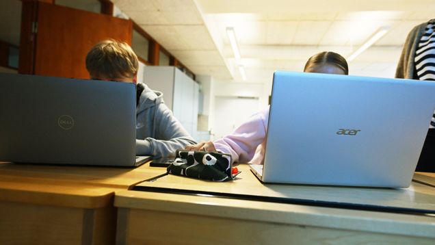 Two pupils using laptops at school desks.