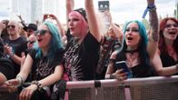 Four young women in black cheering while standing behind a metal barrier.