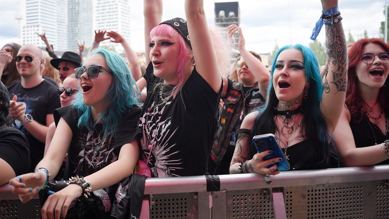 Four young women in black cheering while standing behind a metal barrier.