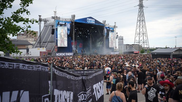 Throngs of people around a big urban outdoor stage with high-tension wires in the background.