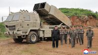 Mustapukuinen Kim Jong-un kävelee sotilasjohdon kanssa liikuteltavan ohjusjärjestelmän vierellä.