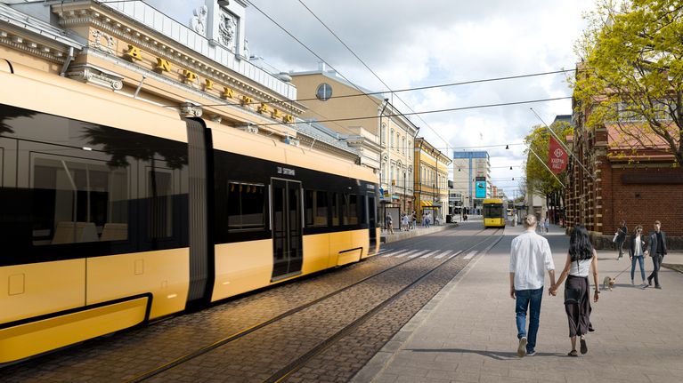 Personer går och cyklar på en livlig stadsplats med spårvagnar i bakgrunden.