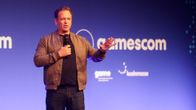 Phil Spencer puhuu mikrofoniin Gamescom-tapahtumassa, taustalla sininen mainosseinä.