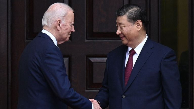 Yhdysvaltain presidentti Joe Biden ja Kiinan presidentti Xi Jinping kättelevät ennen tapaamista, taustalla tumma ovi.