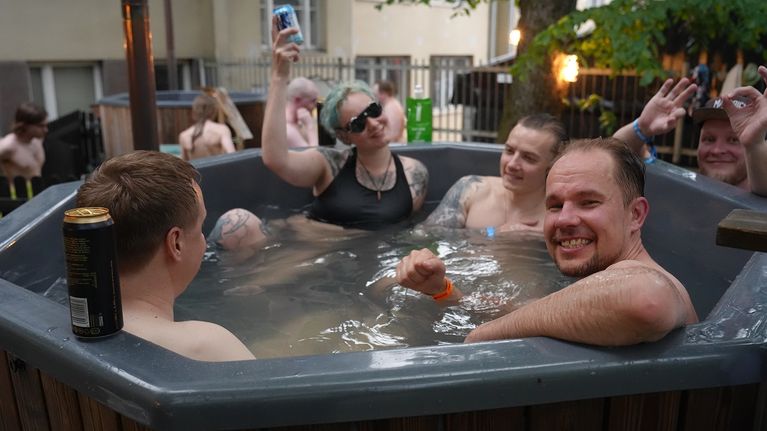 Three men and a woman drinking beer and smiling in an outdoor hot tub.