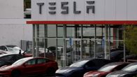 Tummia ja punaisia autoja on pysäköity autokaupan pihaan. Kaupan seinustassa on Tesla-kyltti.