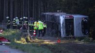 Pelastushenkilöstöä ja viranomaisia on tutkimassa kaatunutta linja-autoa metsän reunassa.