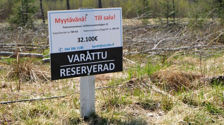 En vit skylt där det står att tomten är till salu. 