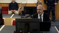 Kuva oikeussalista. Etualalla asianajajamies. Takana nainen, joka peittää kasvonsa ruskean paperikirjeen taakse.