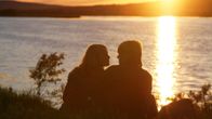 Silhouette of a couple sitting by a lake with golden sun shining on the horizon and the water.