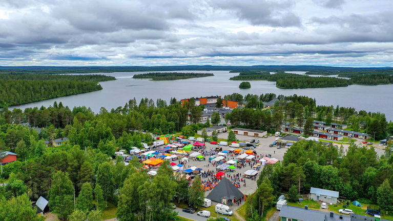Aerial photo of a small village, featuring a lot of stands and people at an outdoor marketplace.