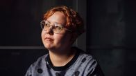 Lähikuvassa nuori nainen, jolla on lyhyet punaiset hiukset, pyöreät kasvot ja silmälasit. Hän katselee kameran ohitse yläviistoon.