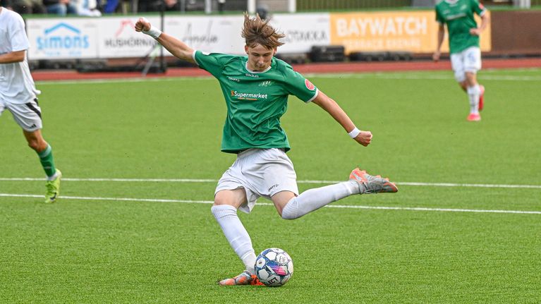 En fotbollsspelare i grön speltröja sparkar iväg bollen.