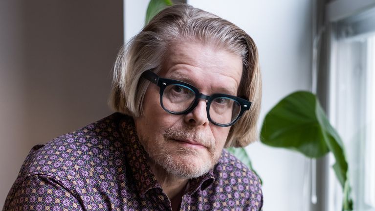 Henkilö seisoo huoneessa viherkasvien vierellä ja katsoo ulos ikkunasta.