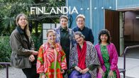 Sju personer poserar för en kamera framför en stor skylt med texten Finlandia.