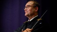 Mies univormussa pitelee kapellimestarin tahtipuikkoa.