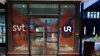 Glasdörrar till en byggnad täckta i röd färg. På dörrarna står det "SVT" och "UR".