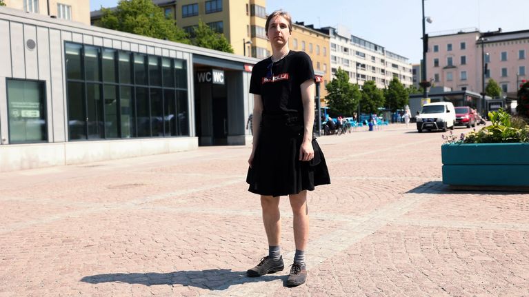Mies seisoo Lahden torilla musta hame ja musta t-paita päällä.