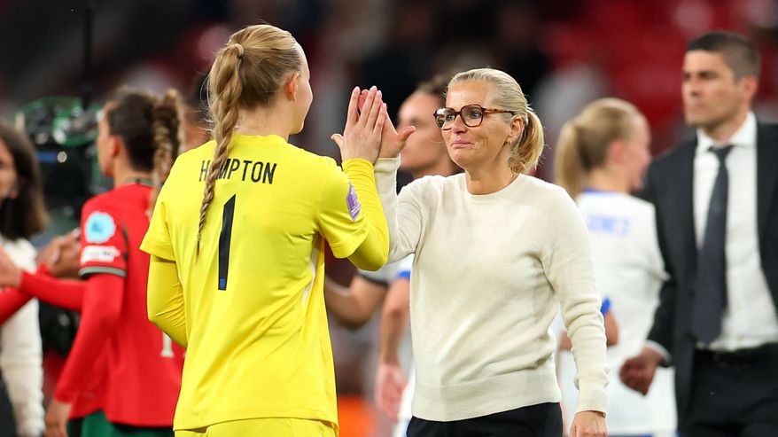 Mary Hampton, pukeutuneena kirkkaankeltaiseen peliasuun, jakaa iloisen hetken toisen henkilön kanssa kentän laidalla jalkapallo-ottelun jälkeen. Taustalla näkyy muita pelaajia ja katsojia.