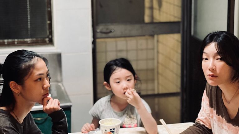 Nuori taiwanilaisnainen, tyttö ja nainen syövät nuudeleita pöydän ääressä.