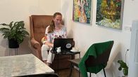 Yksinyrittäjä Liisa Hanén istuu yksin kahvipöydässä helsinkiläisessä kahvilassa kannettava tietokone pöydällä. Taustalla värikkäitä taidemaalauksia.