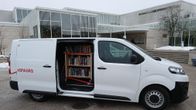 Valkoinen pakettiauto on pysäköitynä rakennuksen edessä.