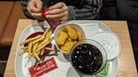 En ung person i beråd att äta en hamburgarmeny. Kärlen är av plast.