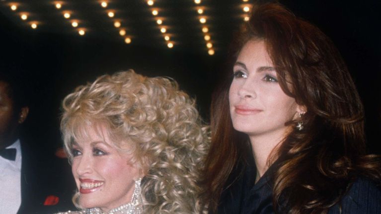 Dolly Parton i en glittrig dräkt bredvid Julia Roberts i svart kostym.