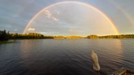 Järven yllä näkyy kirkas sateenkaari ja sen yläpuolella himmeämpi, etualalla puiselta laiturilta erottuu lintupatsas.