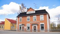 Lähes 120-vuotias, oranssin värinen puutalo, jonka etuseinässä lukee kirjakauppa. Taustalla sininen taivas.