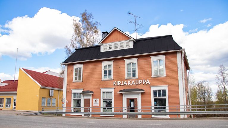 Lähes 120-vuotias, oranssin värinen puutalo, jonka etuseinässä lukee kirjakauppa. Taustalla sininen taivas.