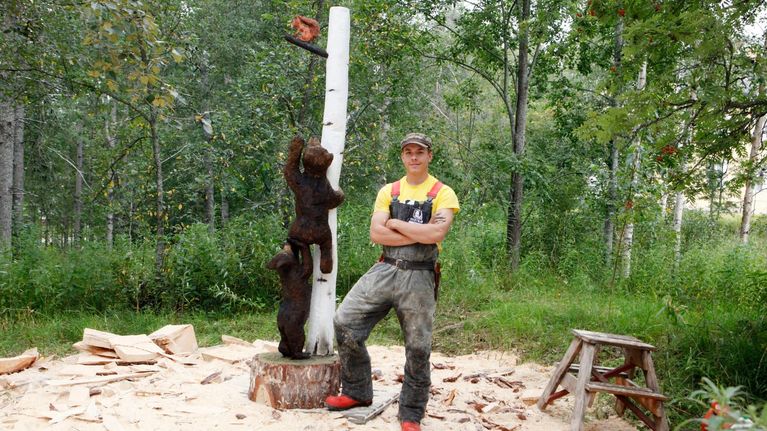 Jani Grönlund poseeraa kunniamaininnan saaneen työnsä vieressä Ilomantsin Karhufestivaaleilla 2020