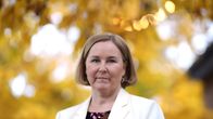 Vaalea polkkatukkainen nainen seisoo kädet ristissä valkoisessa bleiserissä ja katsoo kameraan. Taustalla syysruskaa.