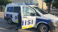 Poliisiauton ovi auki ja autoon on menossa naispoliisi, taustalla näkyy kivitaloja.