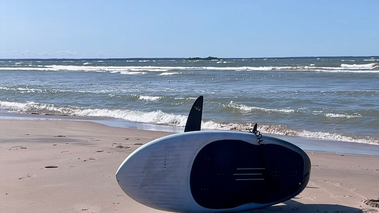 SURF-lauta kyljellään hiekkarannalla meren rannalla, valmiina vesillelähtöön.