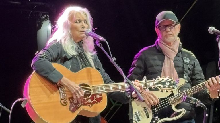 Emmylou harris med gitarr och slutna ögon, på scen.
