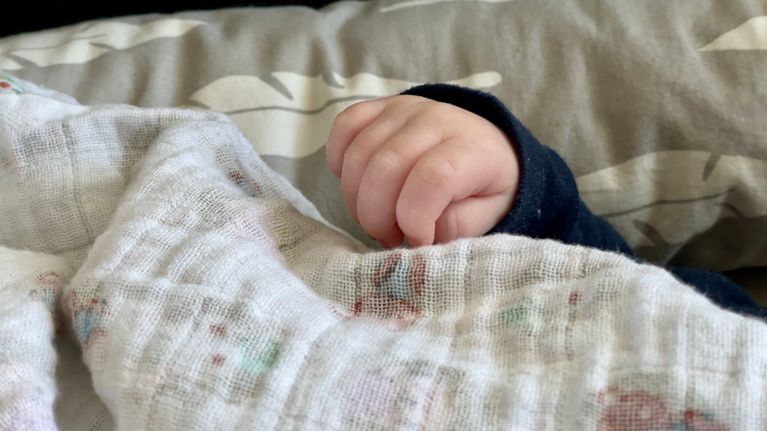 An infant's hand peeks out from a blanket. 
