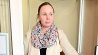 Kvinna med mörkt hår, klädd i ljus jacka kommer ut genom ytterdörren till en skolbyggnad. 