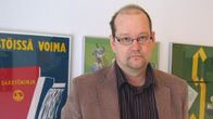 Jaakko Kiander seisoo seinän edessä, seinällä värikkäitä julisteita kehystettyinä.