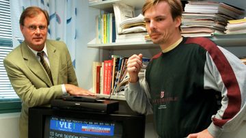Televisiovastaanottimen takana vasemmalla seisoo Jorma Lampinen, teksti-tv:n päällikkö ja oikealla Tapio Vuorinen (2000).