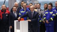 Vladimir Putin kääntääsuurta oranssia kytkintä. Taustalla sinisiin työvaatteisiin ja pukuihin pukeutuneita ihmisiä.