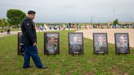En soldat som står utomhus framför flera stora fotografier på soldater med USA:s flagga i bakgrunden.