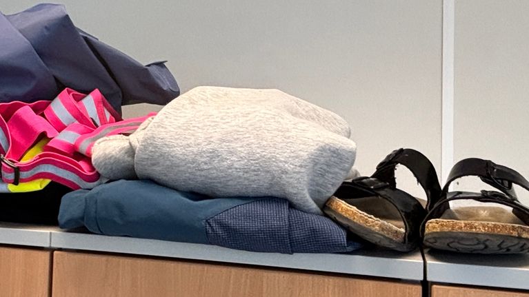 Ett par svarta sandaler och en hög kläder ligger ovanpå ett skåp.