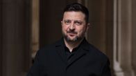 Volodymyr Zelenskyj i en svart skjorta och jacka ler och tittar framåt.