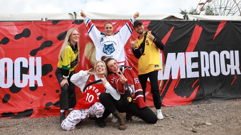 Viisi nuorta poseeraa Simerockin mainosaidan edessä.