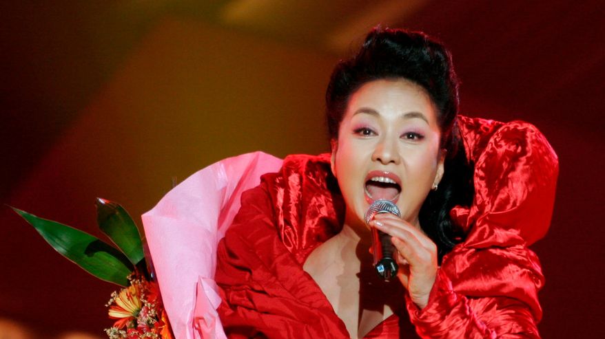 Kirkkaanpunaisessa juhlapuvussa oleva Peng Liyuan laulaa mikrofoni toisessa ja kukkapuska toisessa kädessä. 