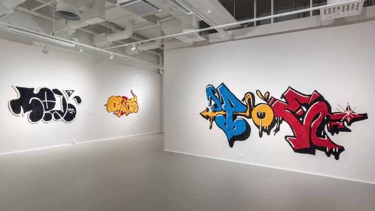 Tuftattuja, graffitia jäljitteleviä ryijyjä taidegallerian seinällä.