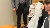 Mustaan huppariin pukeutunut epäilty, joka peittänyt kasvonsa valkoisella t-paidalla.