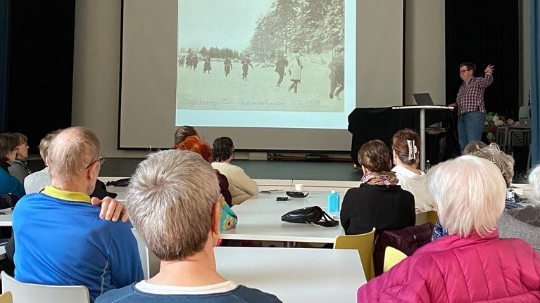 En person håller en presentation framför en sittande publik i en stor sal.