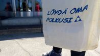 Al-Anonin jäsen seisoo ulkona kangaskassi kädessä.